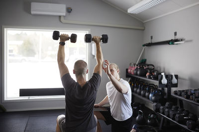 Man exercising with dumbbell with trainer checking his progress