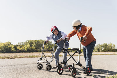 Two old friends wearing safety helmets, competing in a wheeled walker race