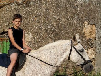 Portrait of young man sitting on rock against wall