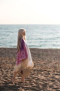 Full length of woman holding basket standing on beach