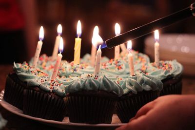 Cropped hand igniting birthday candles on cupcakes in darkroom