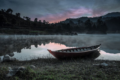 Boat moored on shore by lake against sky