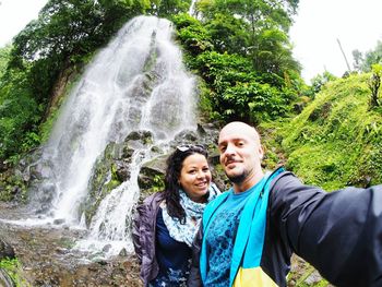 Portrait of smiling young woman standing against waterfall