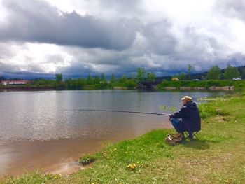 Full length of boy sitting on fishing rod against sky