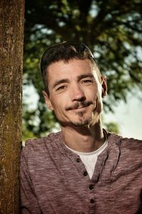 Portrait of mature man smiling while standing against tree