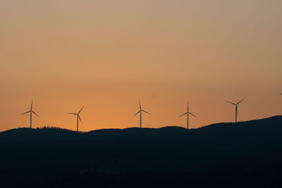 Silhouette wind turbines on hills against sky during sunset