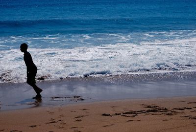 Side view of boy running on sea shore at beach