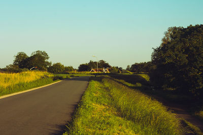 Road amidst field against clear sky