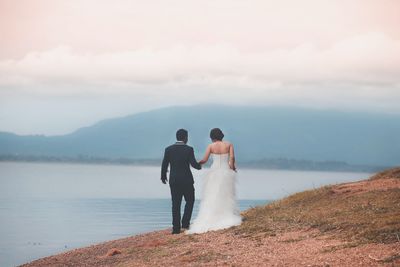 Couple walking at beach against mountains during sunset