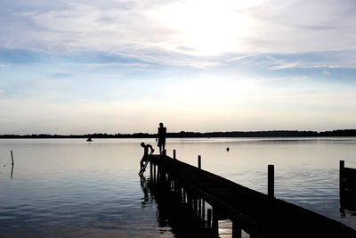 Silhouette people standing on pier over lake against sky during sunset