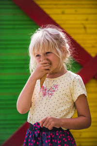 Thoughtful girl eating ice cream cone while standing against wall