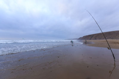 Fishing rod on shore at beach against sky