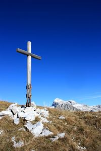 Cross on snow covered landscape against blue sky