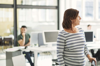 Thoughtful mature businesswoman with male colleague in background at office