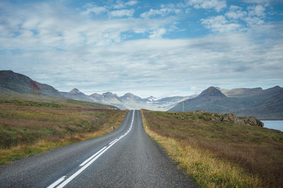 Empty road leading towards mountains against cloudy sky