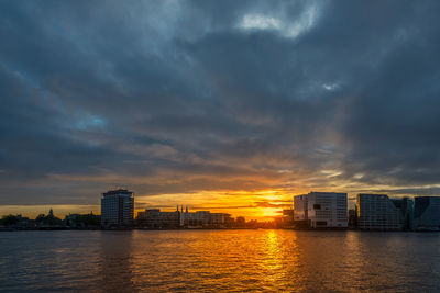 Buildings by river against cloudy sky