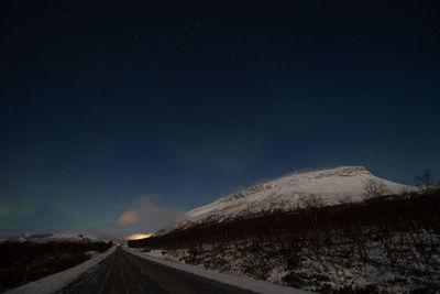 Road by snowcapped mountain against sky at night