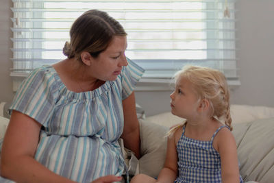 Mother talking with daughter while sitting on sofa