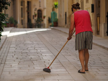 Rear view of woman sweeping alley amidst buildings in town
