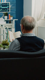 Rear view of senior man reading book sitting on sofa