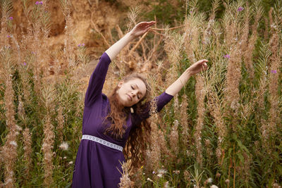 Portrait of young woman with arms raised standing on field