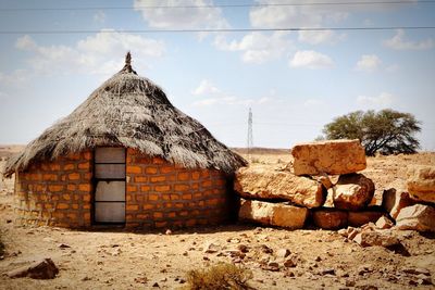 Thatched roof house on arid landscape against sky during sunny day