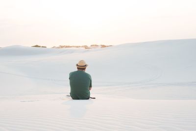 Rear view of man sitting on sand dune against clear sky
