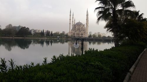 Mosque by reflection lake against sky