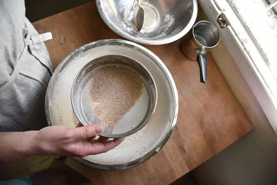 A female cook in apron sifts flour in a metal bowl