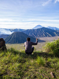 Rear view of man crouching against mountains