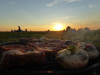 Close-up of meat on barbecue grill against sky during sunset