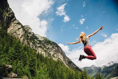 Young woman jumping on mountain against sky