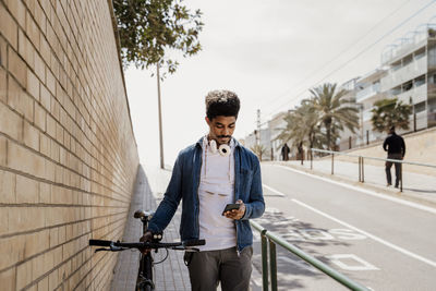 Handsome man using mobile phone while standing with bicycle on footpath