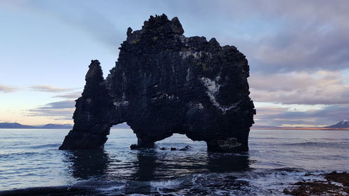 Rock formation on beach against sky during sunset