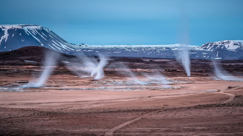 Scenic view of hot springs emitting smoke by snow covered mountains against sky