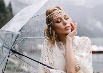 A tender sensual young woman bride in a fashionable wedding dress is standing in the rain in nature