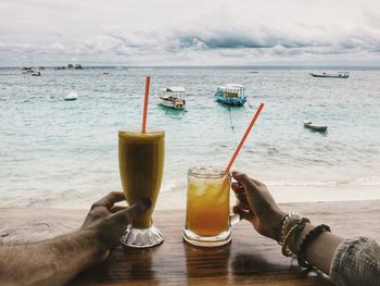 Cropped image of hands with drinks at beach