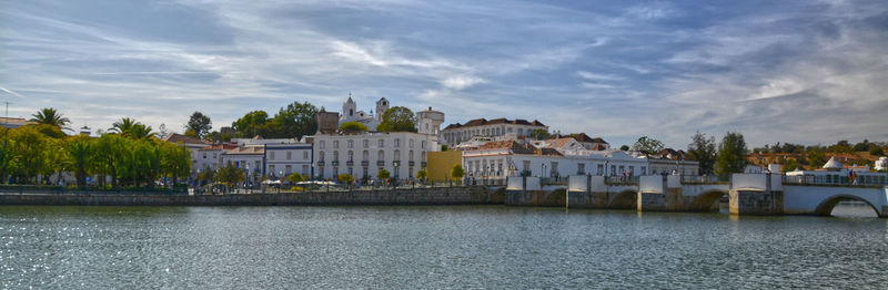 Buildings at waterfront against cloudy sky