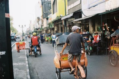 Rear view of man riding pedicab on city street