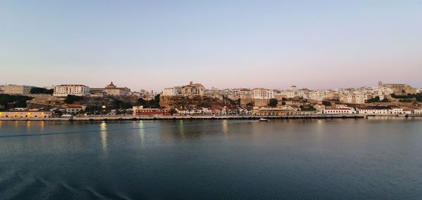 City by river against sky at dusk