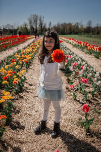 Girl in white top stands in tulip field holding big orange flower