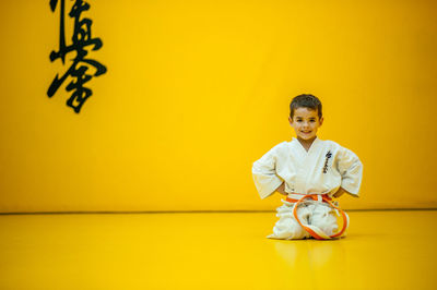 Portrait of cute boy practicing martial arts against yellow wall