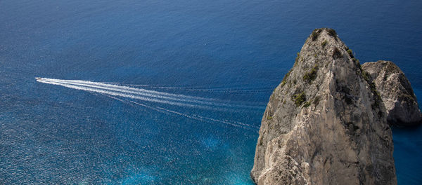 Aerial view of rocks by sea against blue sky