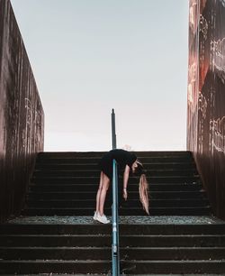 Low angle view of woman on staircase against clear sky