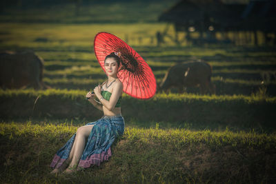 Portrait of woman with umbrella sitting on land