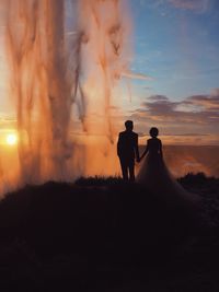 Bride and groom standing against geyser during sunset