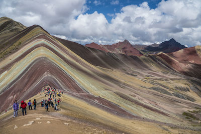 Hikers on mountain against cloudy sky
