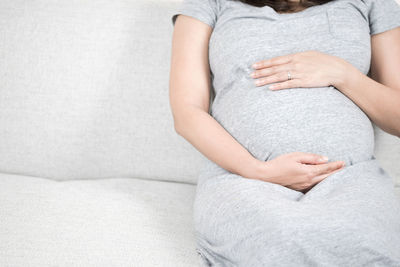 Midsection of pregnant woman sitting on sofa at home