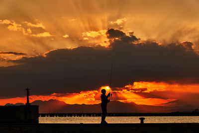 Silhouette people standing on beach against sky during sunset