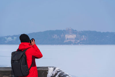 Rear view of man photographing against sky during winter